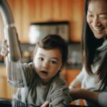 Mother and child washing hands together in a warm and joyful kitchen moment, fostering love and cleanliness.