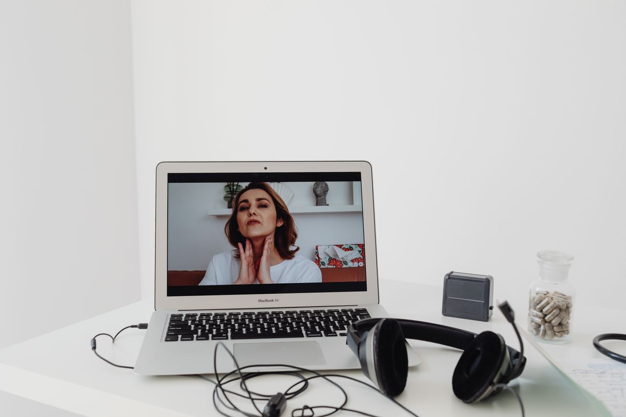 A woman conducting a telemedicine session visible on a laptop screen with headphones nearby.